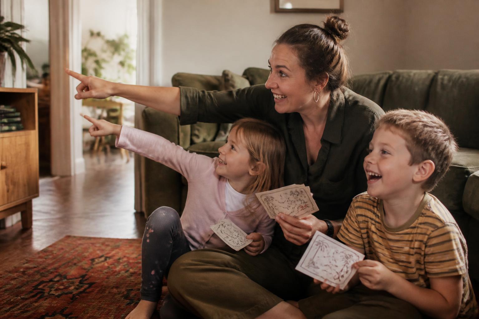 A parent and two children sitting on the floor together, holding clue cards and pointing